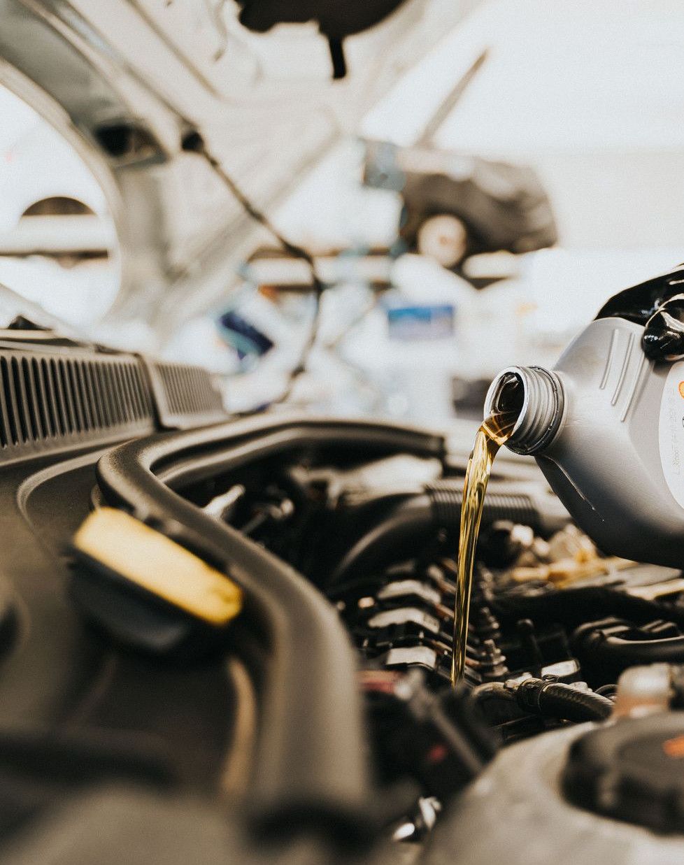 Close-up of a mechanic pouring engine oil into a car engine in an auto repair shop.