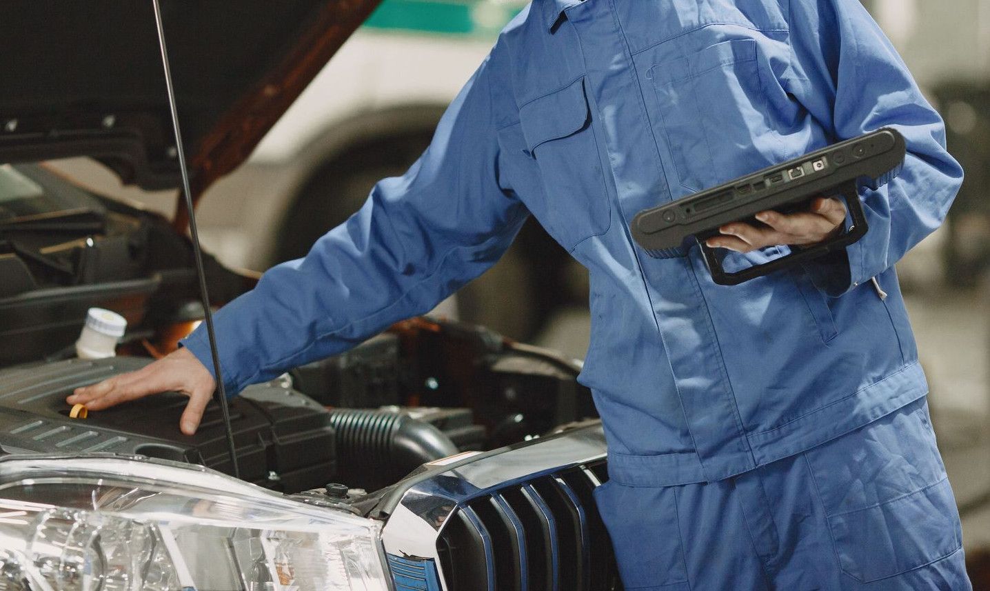 Professional mechanic examining a car engine under an open hood in a garage setting.
